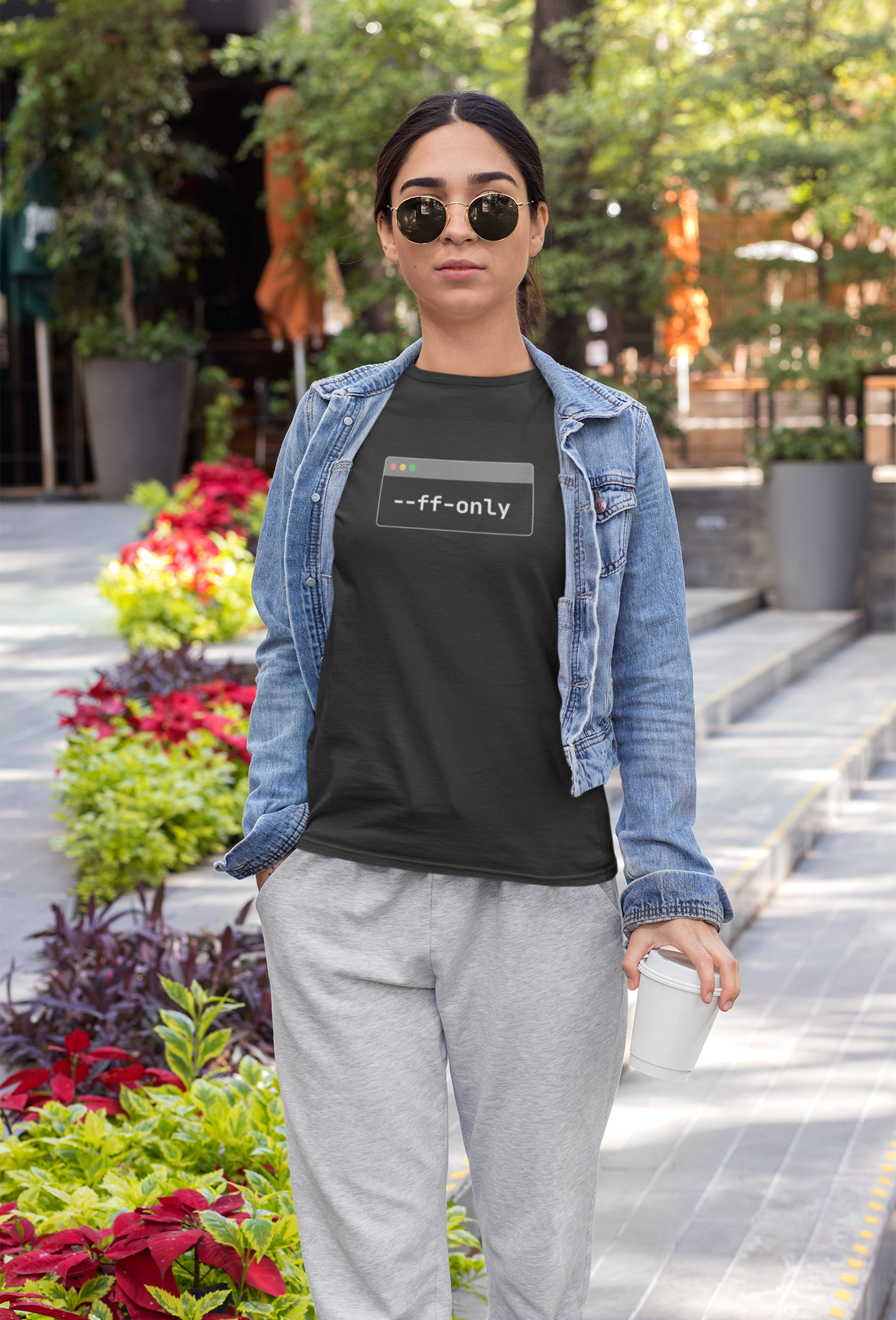 Person wearing a black t-shirt with text, denim jacket, and gray pants in an outdoor setting.