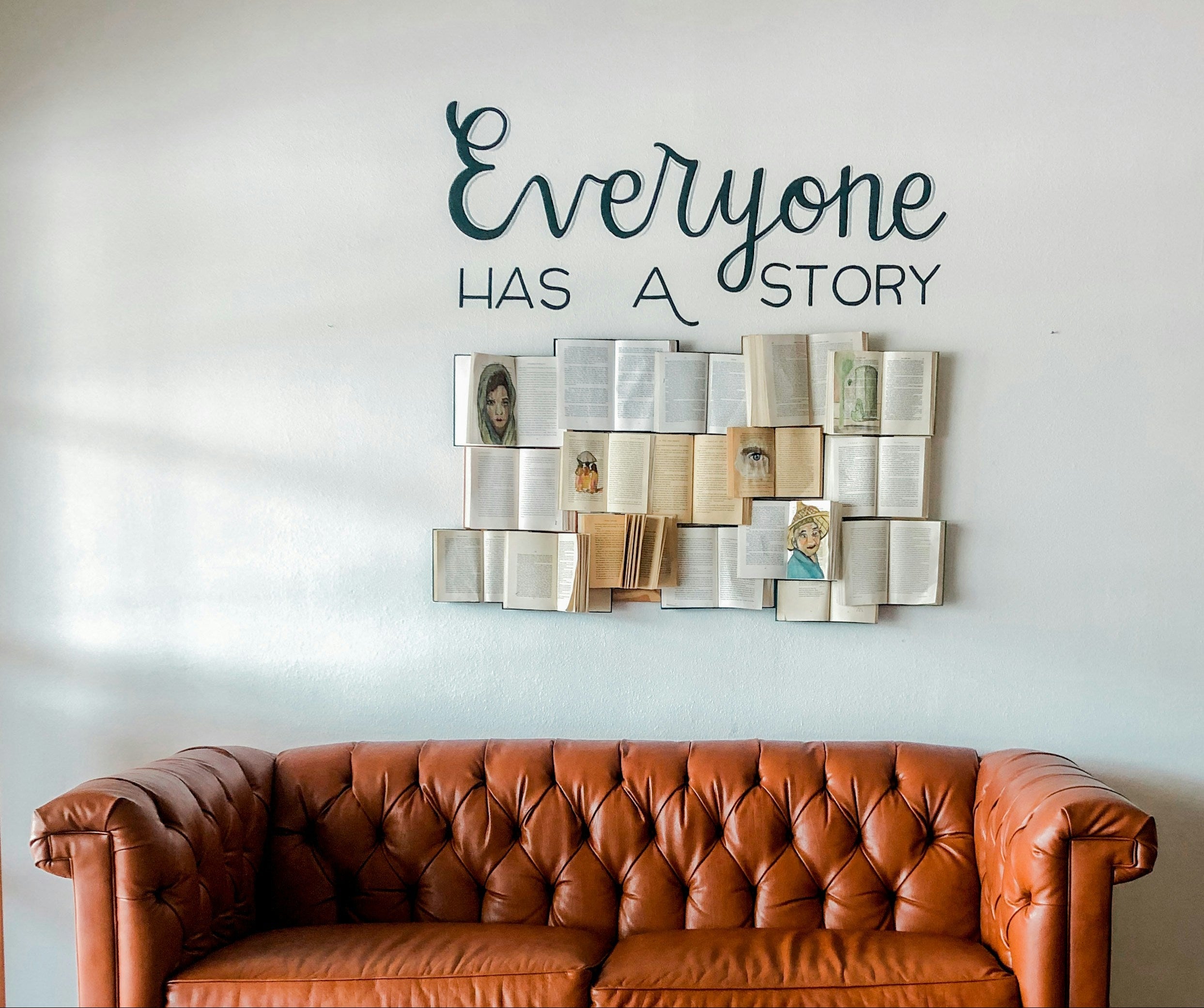 Brown leather sofa in front of a wall with 'Everyone has a story' quote and book art.