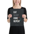Product mockup- Person holding a black poster with 'EAT SLEEP CODE REPEAT' text.