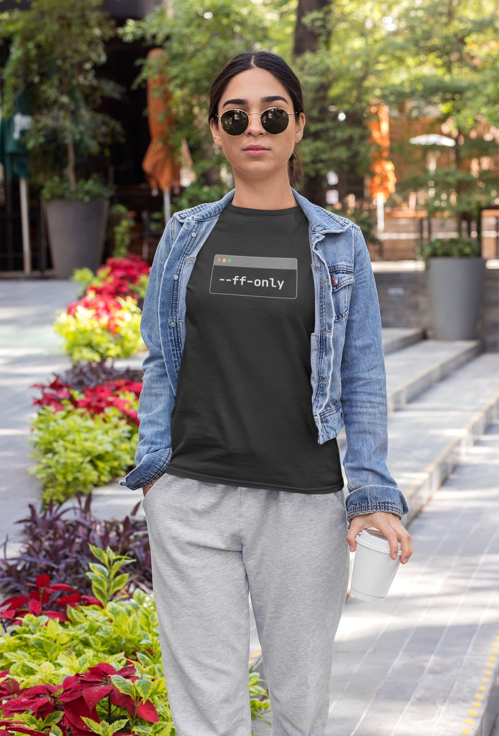 Person wearing a black t-shirt with text, denim jacket, and gray pants in an outdoor setting.
